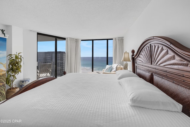 bedroom featuring a wall of windows, a water view, a textured ceiling, and access to exterior