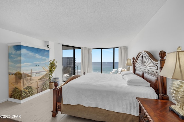 bedroom with access to outside, expansive windows, a textured ceiling, wood finished floors, and baseboards