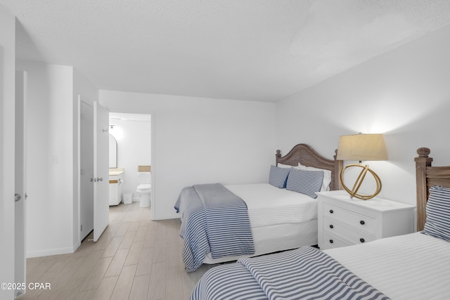 bedroom featuring baseboards, ensuite bath, and light wood-style flooring