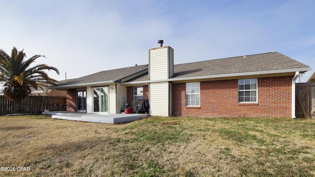 back of house with brick siding, fence, a yard, a chimney, and a patio area