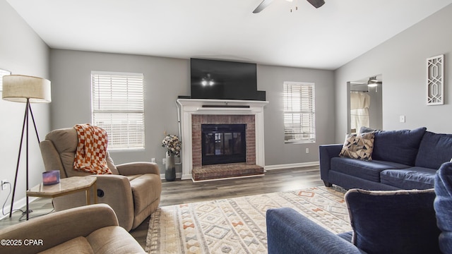 living area featuring lofted ceiling, wood finished floors, a ceiling fan, baseboards, and a brick fireplace