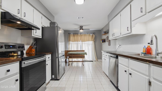 kitchen featuring light tile patterned floors, dark countertops, appliances with stainless steel finishes, a sink, and under cabinet range hood