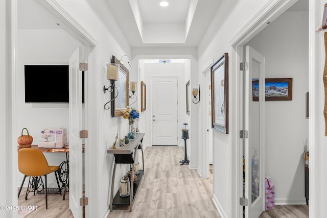 corridor featuring light wood-style flooring, baseboards, and a tray ceiling