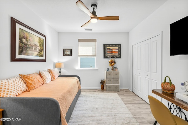 bedroom with baseboards, visible vents, light wood finished floors, ceiling fan, and a closet