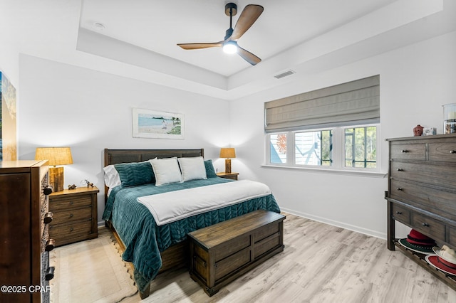 bedroom featuring baseboards, a ceiling fan, light wood-style floors, visible vents, and a raised ceiling