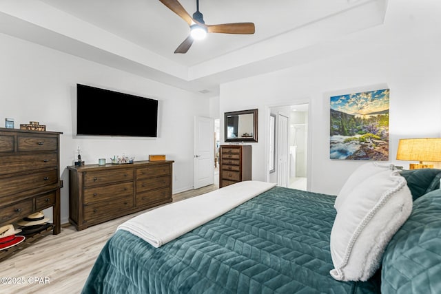 bedroom featuring a tray ceiling, light wood-type flooring, ensuite bath, and a ceiling fan