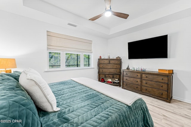 bedroom featuring visible vents, baseboards, light wood-style floors, a raised ceiling, and ceiling fan