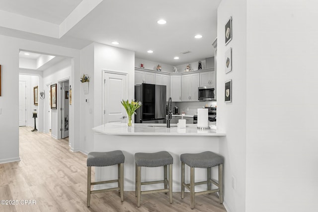 kitchen featuring light wood-type flooring, a breakfast bar, recessed lighting, stainless steel appliances, and a peninsula