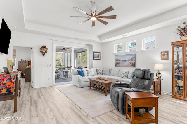 living area featuring a tray ceiling, baseboards, light wood finished floors, and ceiling fan