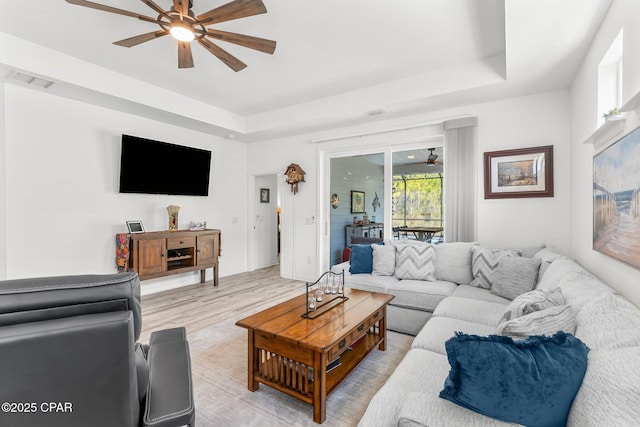 living area with a raised ceiling, light wood finished floors, a ceiling fan, and visible vents
