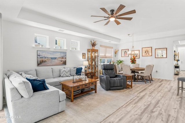 living area featuring light wood finished floors, visible vents, baseboards, a tray ceiling, and a ceiling fan