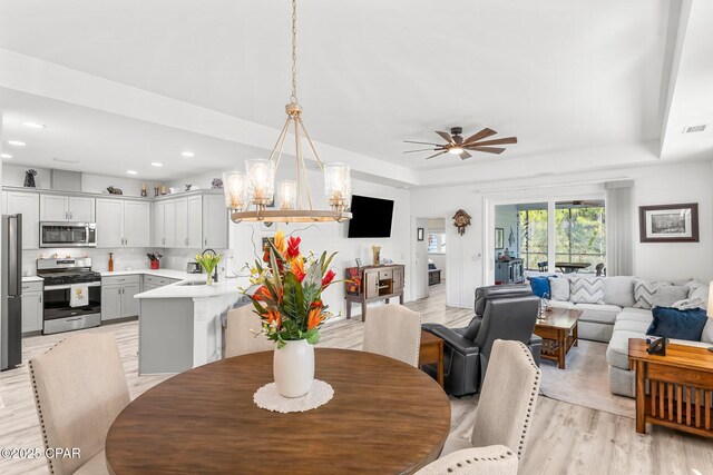 dining room with visible vents, ceiling fan, a tray ceiling, recessed lighting, and light wood-style flooring