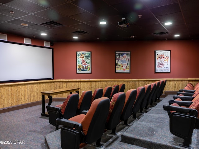 carpeted home theater room featuring a drop ceiling and wood walls