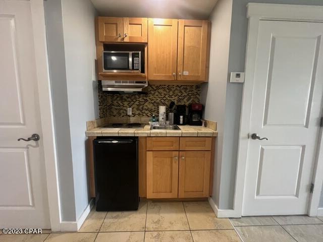 kitchen featuring sink, tasteful backsplash, black appliances, light tile patterned flooring, and tile countertops