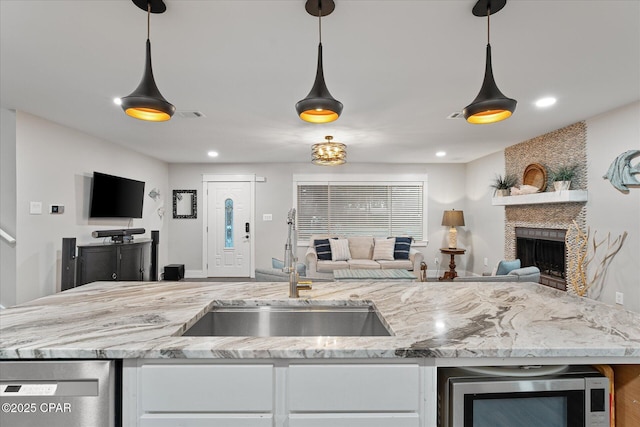 kitchen featuring sink, hanging light fixtures, a large fireplace, stainless steel appliances, and light stone countertops