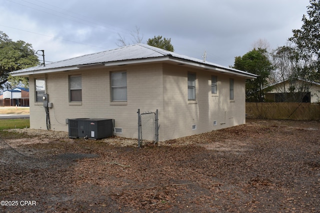view of side of home featuring cooling unit, crawl space, metal roof, fence, and brick siding