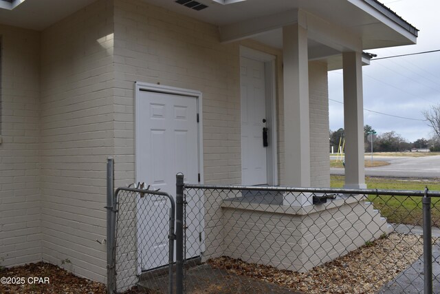 doorway to property featuring brick siding, a porch, fence, and a gate