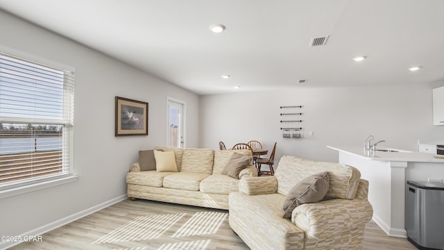 living room featuring sink, light wood-type flooring, and a wealth of natural light