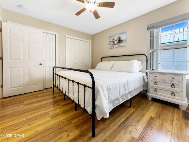 bedroom with two closets, light hardwood / wood-style flooring, and ceiling fan