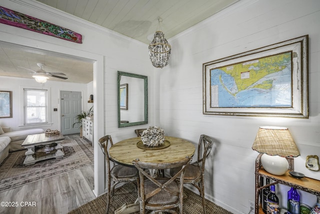 dining area with crown molding, wood-type flooring, wooden walls, and ceiling fan