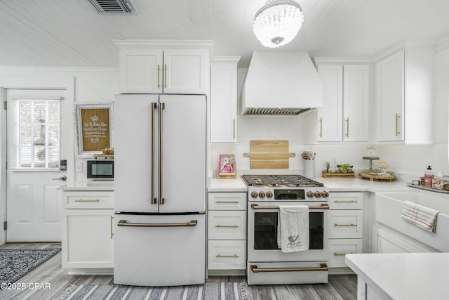 kitchen featuring white cabinetry, high quality appliances, hardwood / wood-style floors, and custom exhaust hood