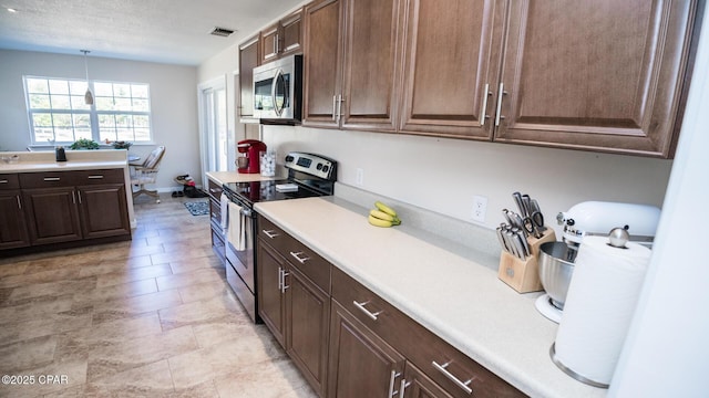 kitchen featuring hanging light fixtures, dark brown cabinets, stainless steel appliances, and a textured ceiling