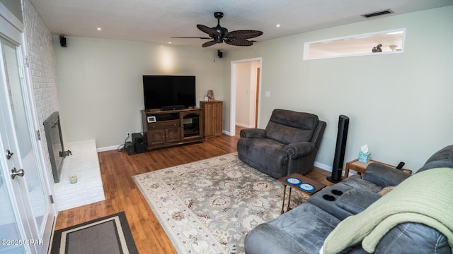 living room with hardwood / wood-style flooring, ceiling fan, and a brick fireplace