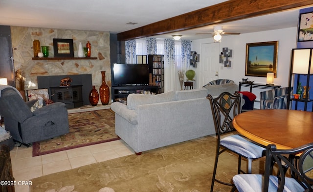 living room with ceiling fan, a wood stove, light tile patterned floors, and beam ceiling