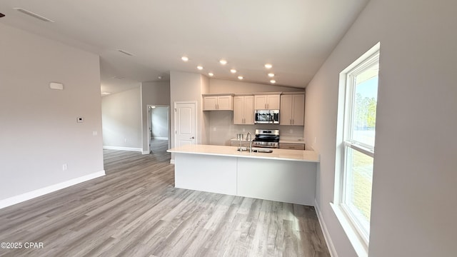 kitchen featuring lofted ceiling, sink, light hardwood / wood-style flooring, a center island with sink, and appliances with stainless steel finishes