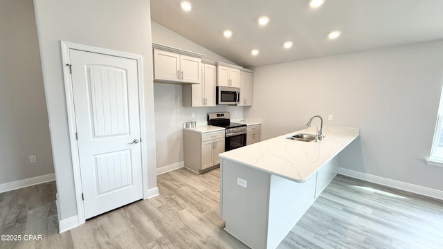 kitchen featuring lofted ceiling, sink, kitchen peninsula, stainless steel appliances, and light hardwood / wood-style floors