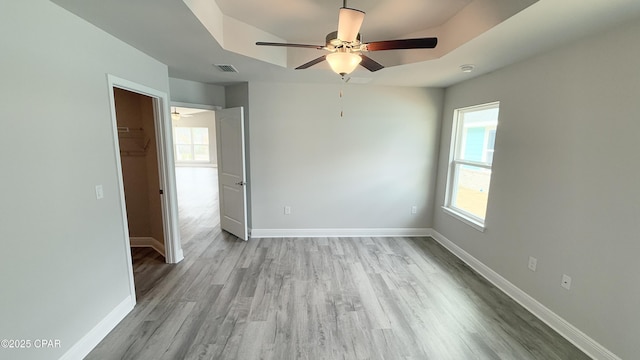 spare room with a tray ceiling, ceiling fan, and light hardwood / wood-style flooring