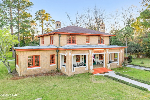 view of front facade featuring a front yard, a porch, brick siding, and a chimney