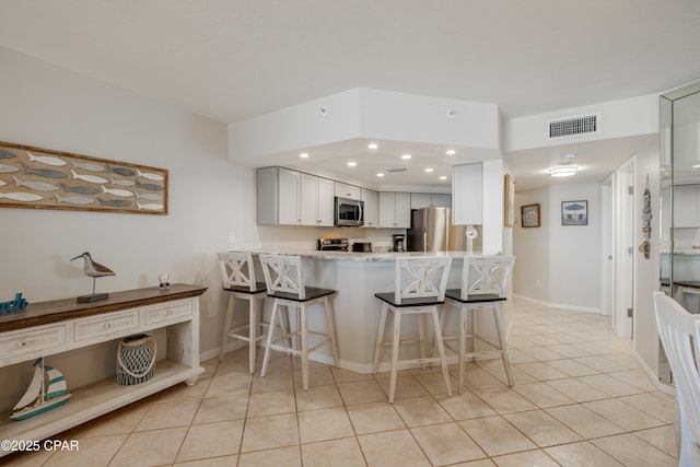 kitchen with white cabinetry, a breakfast bar area, light tile patterned floors, kitchen peninsula, and stainless steel appliances