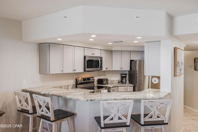 kitchen with appliances with stainless steel finishes, gray cabinetry, a kitchen breakfast bar, and kitchen peninsula