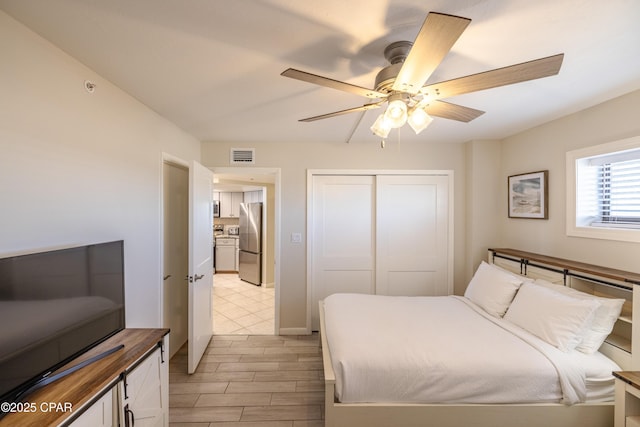 bedroom featuring a closet, light hardwood / wood-style floors, stainless steel refrigerator, and ceiling fan