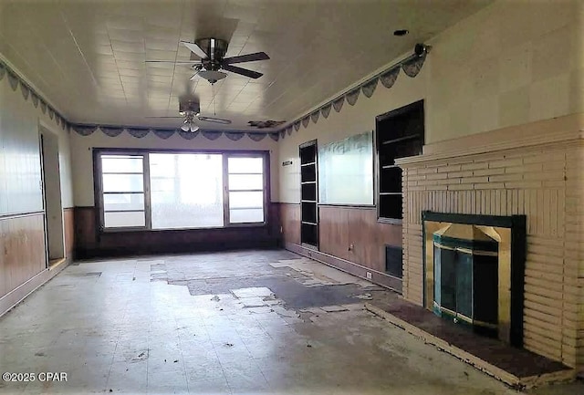 unfurnished living room with ceiling fan, wooden walls, and a brick fireplace