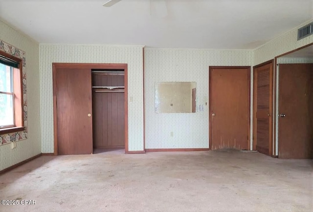 unfurnished bedroom with ceiling fan, light colored carpet, and multiple closets