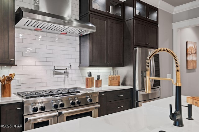22207 Fox Glenn Trce, Panama City Beach, FL 32413 - kitchen featuring appliances with stainless steel finishes, wall chimney range hood, backsplash, light countertops, and dark brown cabinets