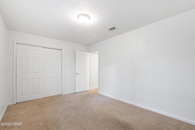 unfurnished bedroom with light colored carpet, a textured ceiling, and a closet