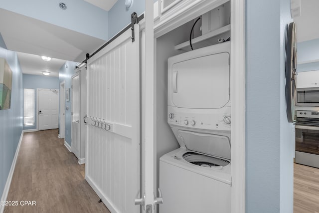 washroom featuring stacked washer and dryer, a barn door, and light wood-type flooring