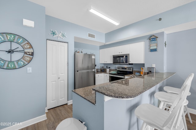 kitchen with appliances with stainless steel finishes, white cabinetry, a kitchen bar, kitchen peninsula, and light hardwood / wood-style flooring