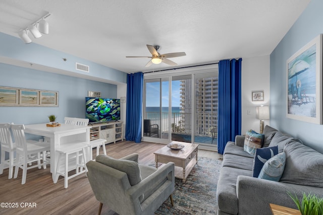 living room with hardwood / wood-style flooring, ceiling fan, rail lighting, and a textured ceiling