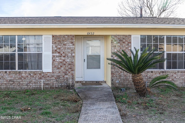 doorway to property with a shingled roof and brick siding