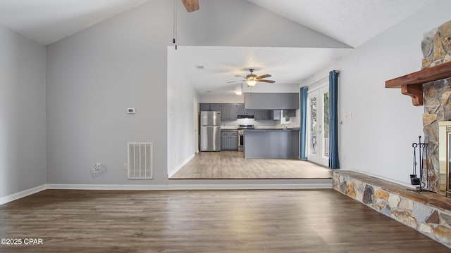 unfurnished living room with hardwood / wood-style floors, a stone fireplace, vaulted ceiling, and ceiling fan