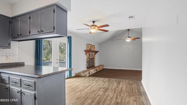 kitchen featuring light hardwood / wood-style flooring, gray cabinetry, tasteful backsplash, a stone fireplace, and vaulted ceiling