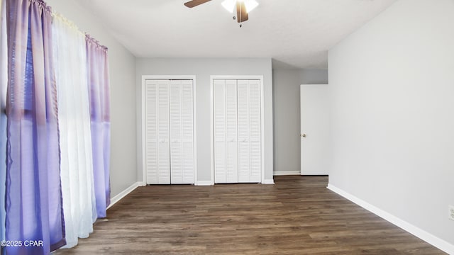 unfurnished bedroom featuring ceiling fan, two closets, and dark hardwood / wood-style flooring