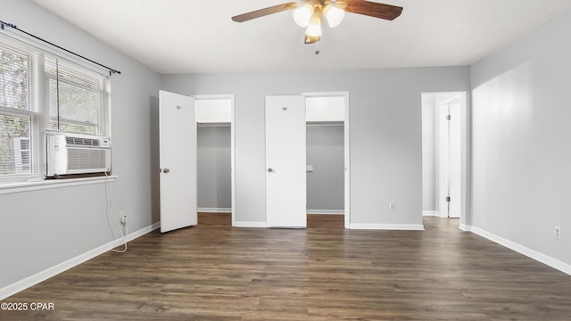 unfurnished bedroom featuring cooling unit, a spacious closet, dark wood-type flooring, and ceiling fan