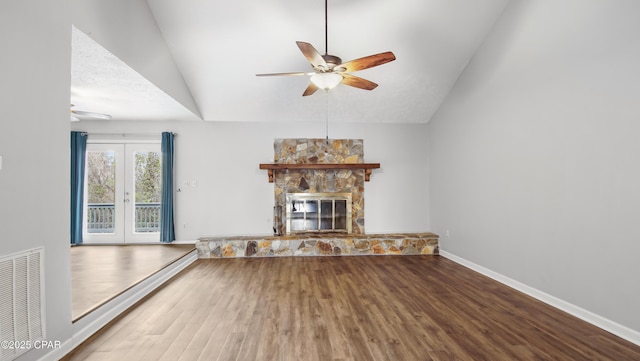 unfurnished living room featuring ceiling fan, hardwood / wood-style floors, a stone fireplace, vaulted ceiling, and french doors