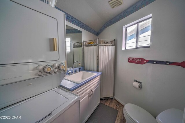 bathroom featuring hardwood / wood-style floors, stacked washer and clothes dryer, vanity, vaulted ceiling, and toilet