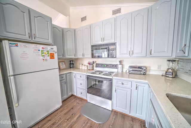 kitchen with vaulted ceiling, sink, light stone countertops, white appliances, and light hardwood / wood-style flooring